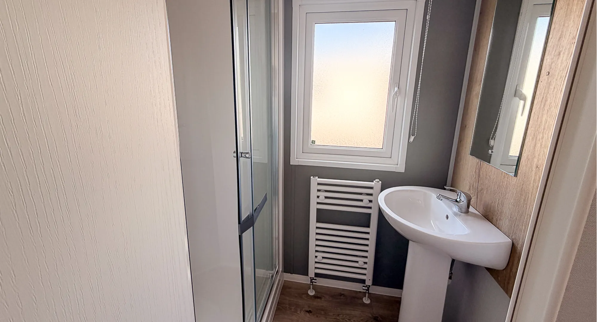 Main bathroom with built in shower and sliding glass door, toilet, vertical radiator and window with wooden floors