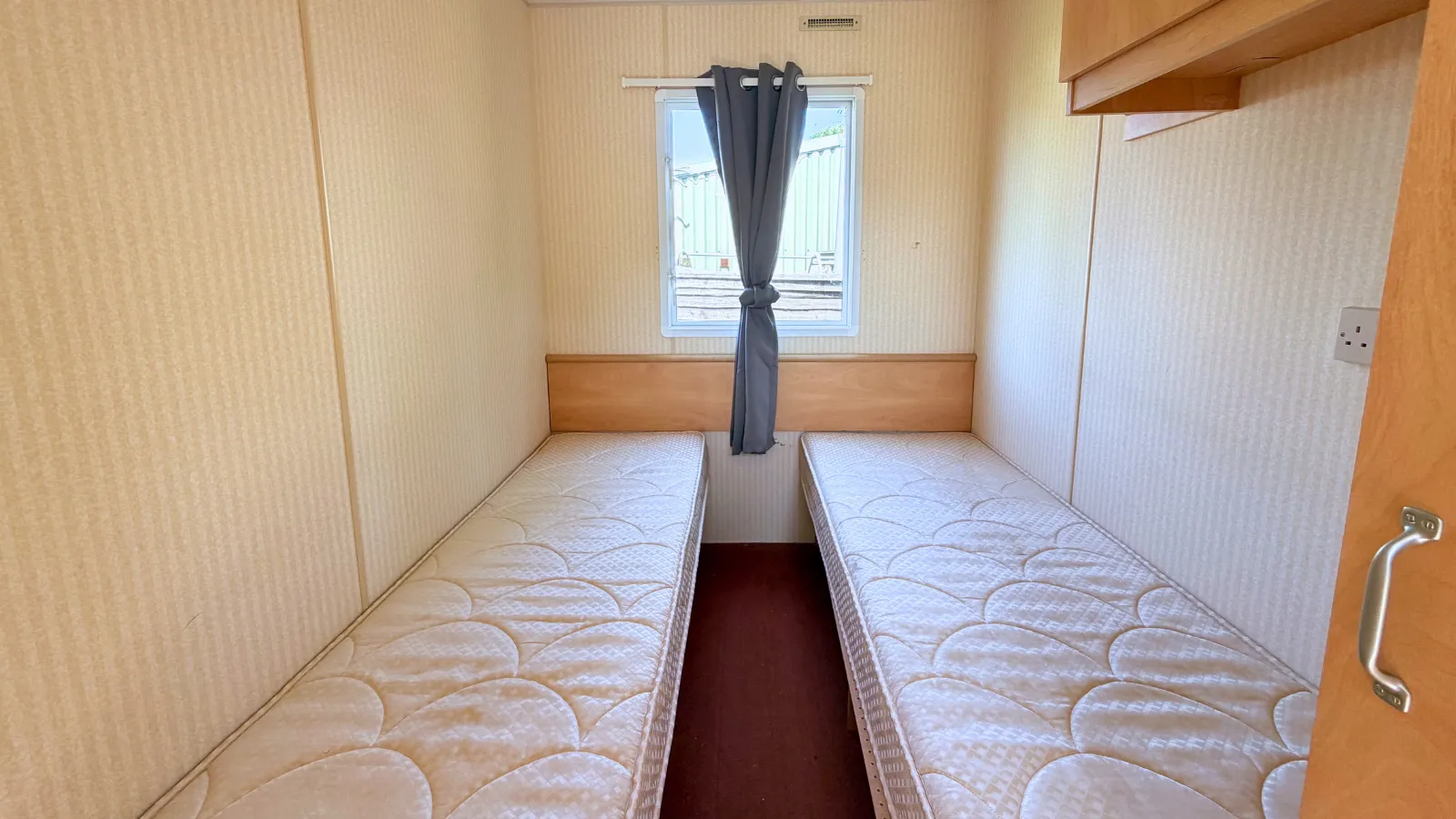 interior view of a bedroom with two single beds and a window in-between and overhead storage