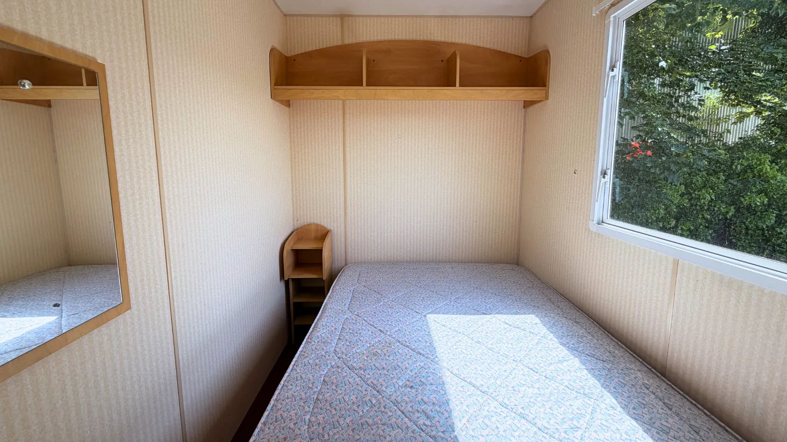 interior view of static caravan with a double bed, overhead shelfing, a night table and a mirror on the wall