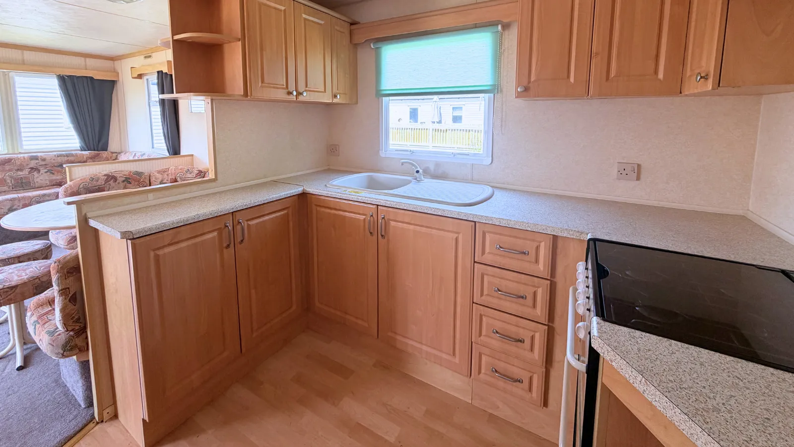 An inside view of a static caravan kitchen are showing oak cupboards and drawers with a built-in sink with drainer and faucet