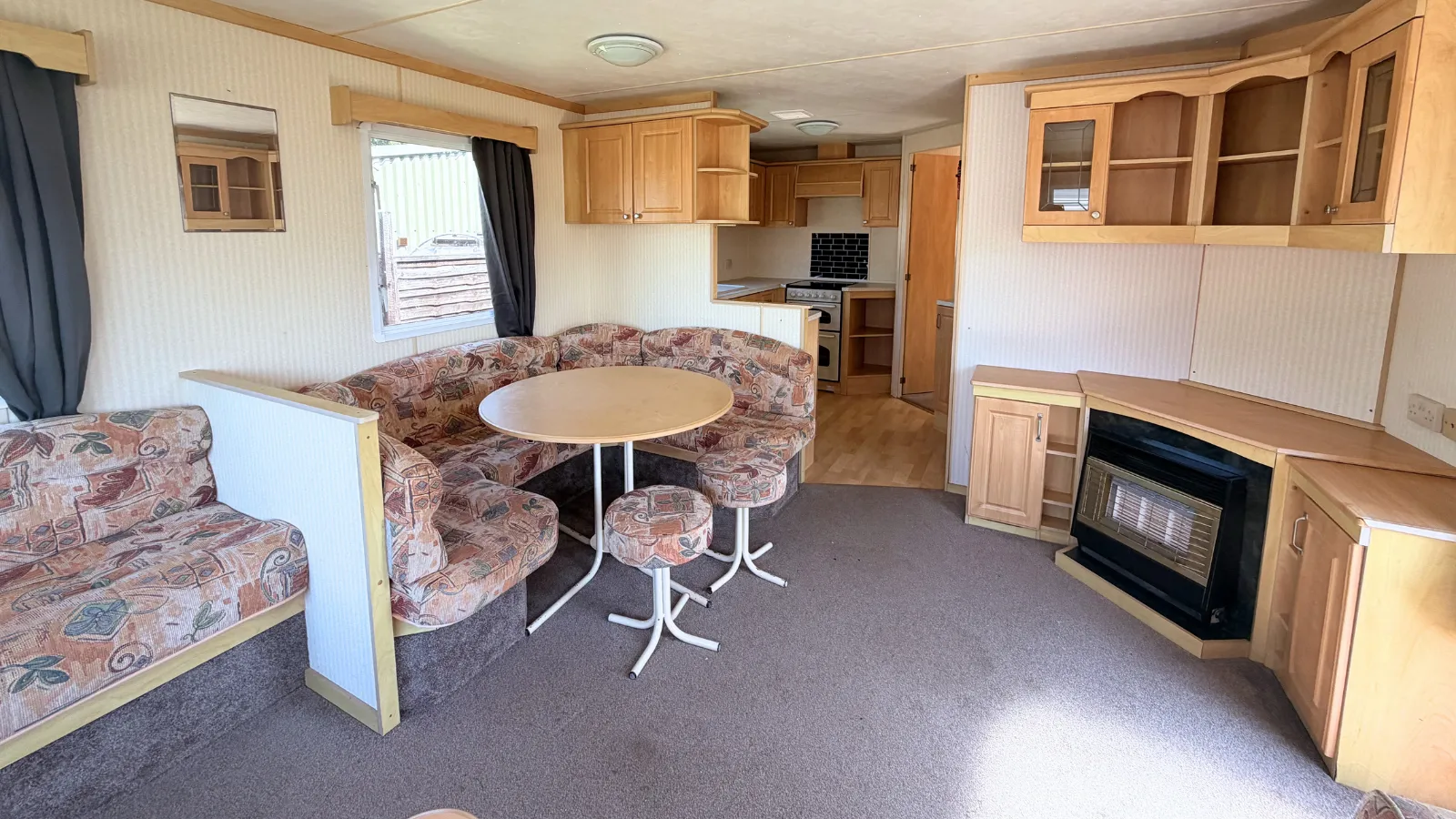 An interior view of a static caravan for sale with a view of a dining area with built in seating, a dining table and two stools with a view behind of a kitchen area