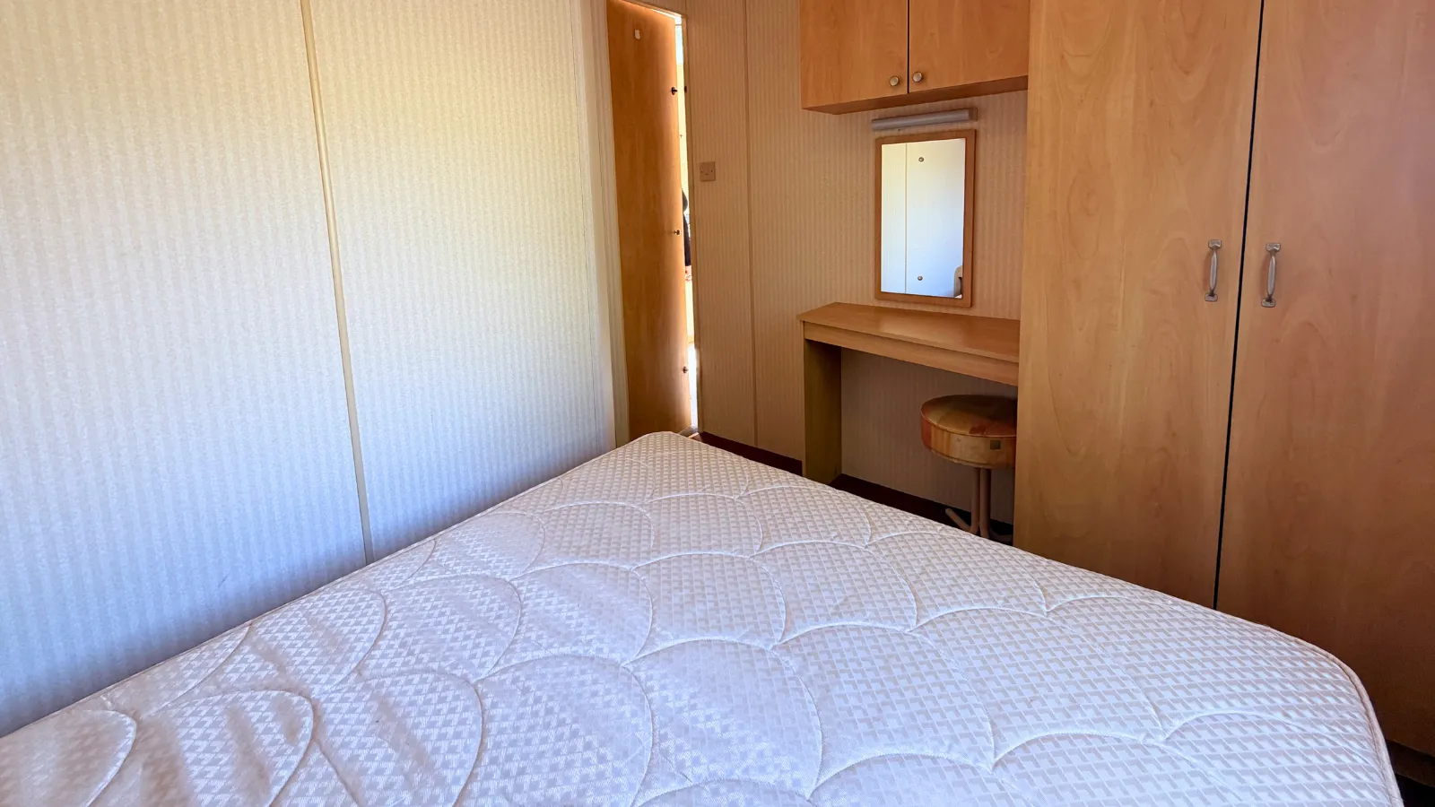 An interior view of a static caravan bedroom with a large bed , built in wardrobe and dressing table with mirror