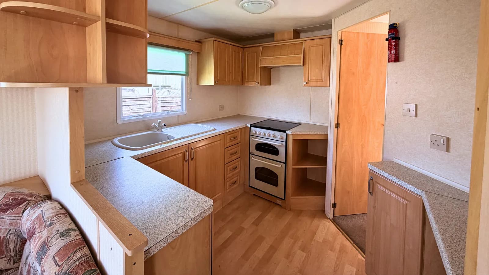 interior view of a static caravan kitchen showing oak cupboards, a double oven and electric cooker, countertops and sink with drainer