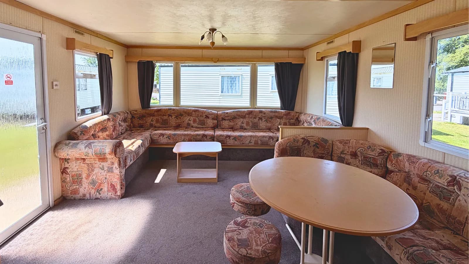 Interior view of a static caravan for sale, with bench seating, a coffee table and dining table with a large bay window to the rear
