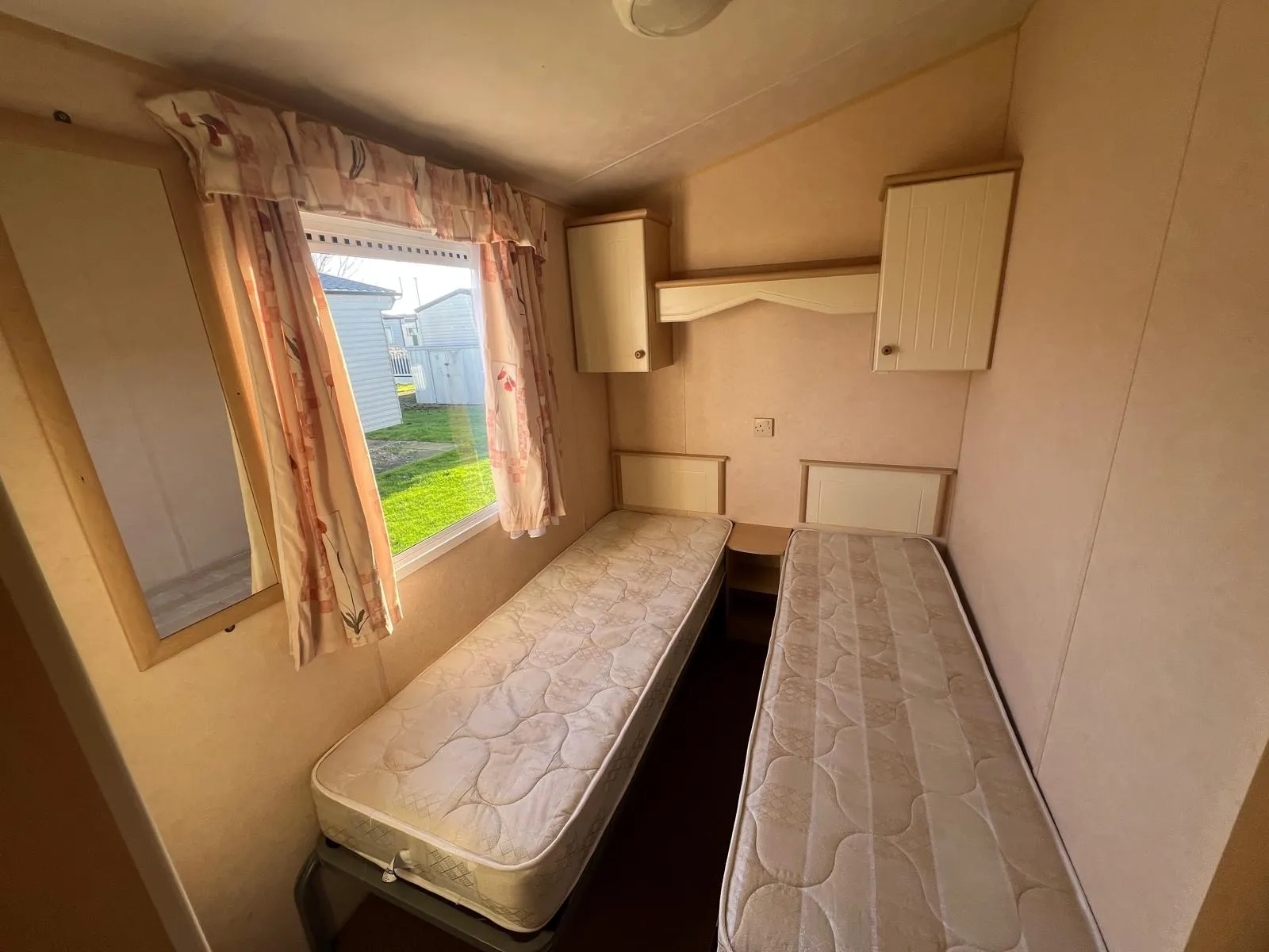 a static caravan bedroom with two single beds and overhead storage with a window to the side