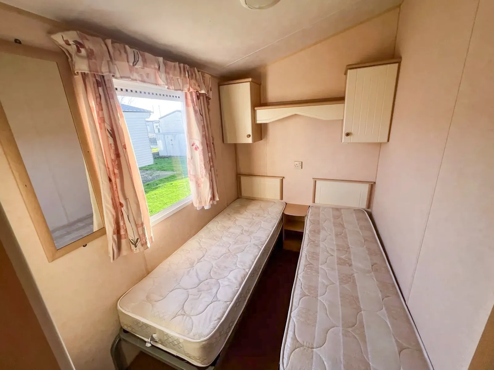 a static caravan bedroom with two single beds and overhead storage with a window to the side