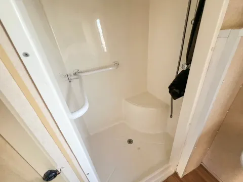 a built in shower unit in whit with a disability handle and a built in seat